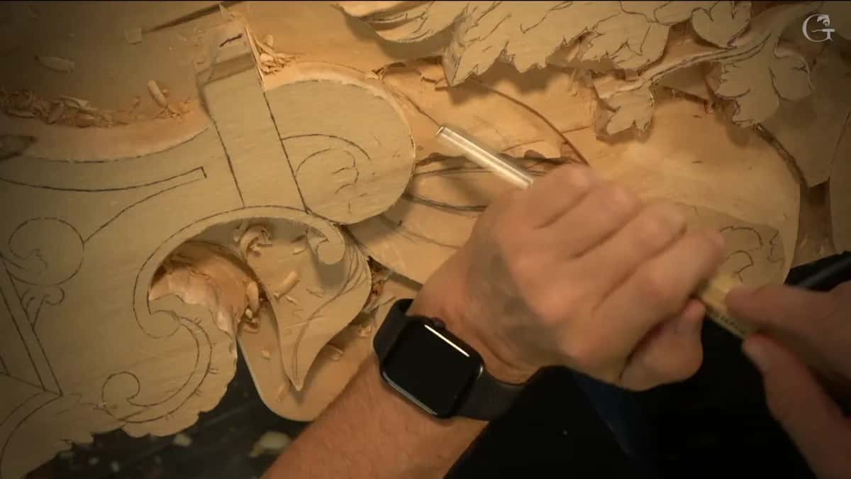 Both hands steer a narrow gouge right underneath the upper line of one ray, with the scroll to the left.