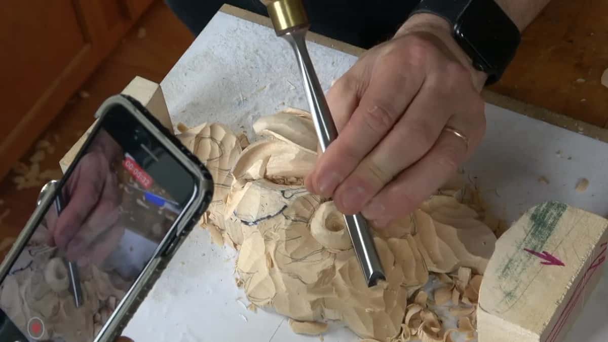 A phone propped at the edge of the bench, recording, while the gouge carries on working