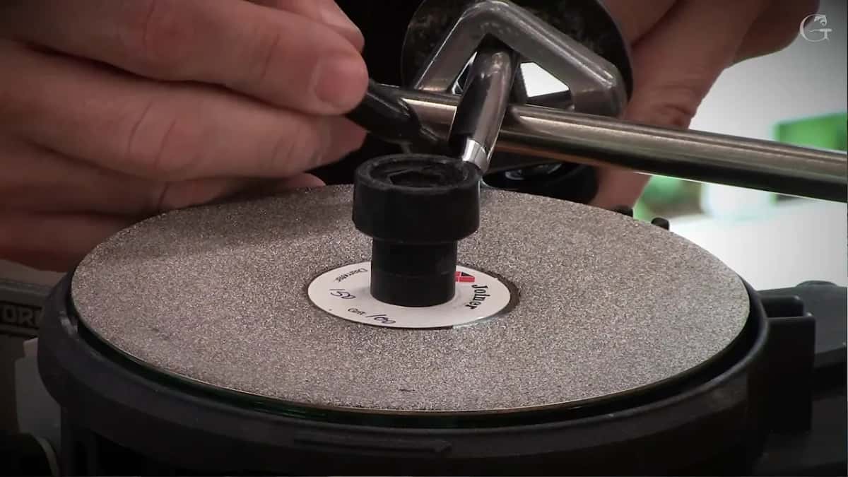 Two hands settle a small gouge down into the jig above the coarse grey disc