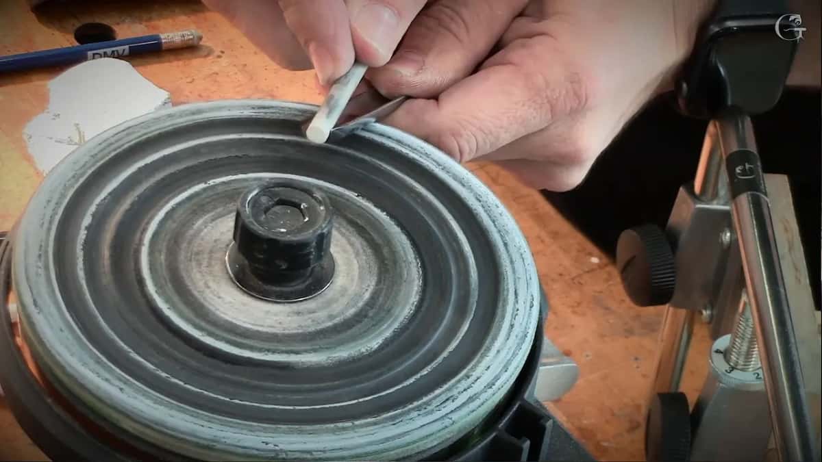 Fingers press a small white ceramic slip against the rim of the wheel