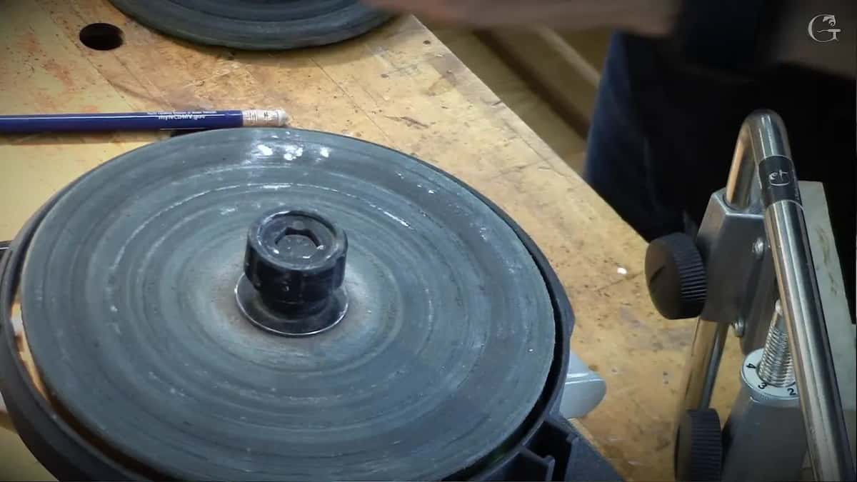 Dark honing wheel mounted and turning, a spare disc and a pencil on the bench behind