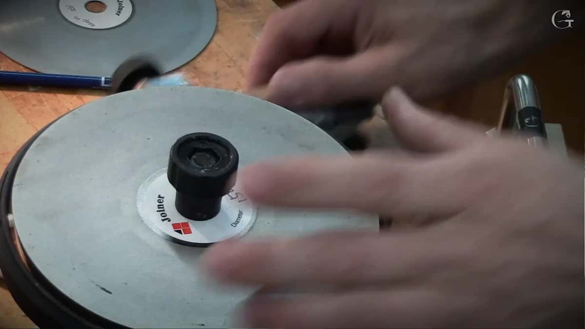 Hands lifting one abrasive disc off its hub while the next one waits on the bench behind