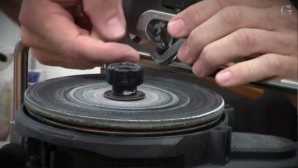 Both hands rest on the Tormek jig as the blade comes down onto the face of a wheel worn right into rings