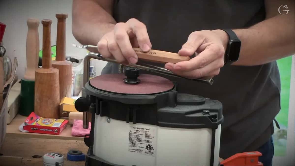 Standing at the Work Sharp with a maroon disc turning, a tool with a turned handle held across the bar, mallets behind
