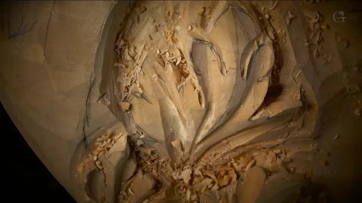 Pencil lines still show on a tall carved leaf, with fresh chips piled at its base and one small dark hollow.