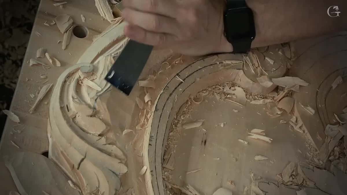 Wide, nearly flat blade held down by the fingers beside the curl, a watch on the wrist