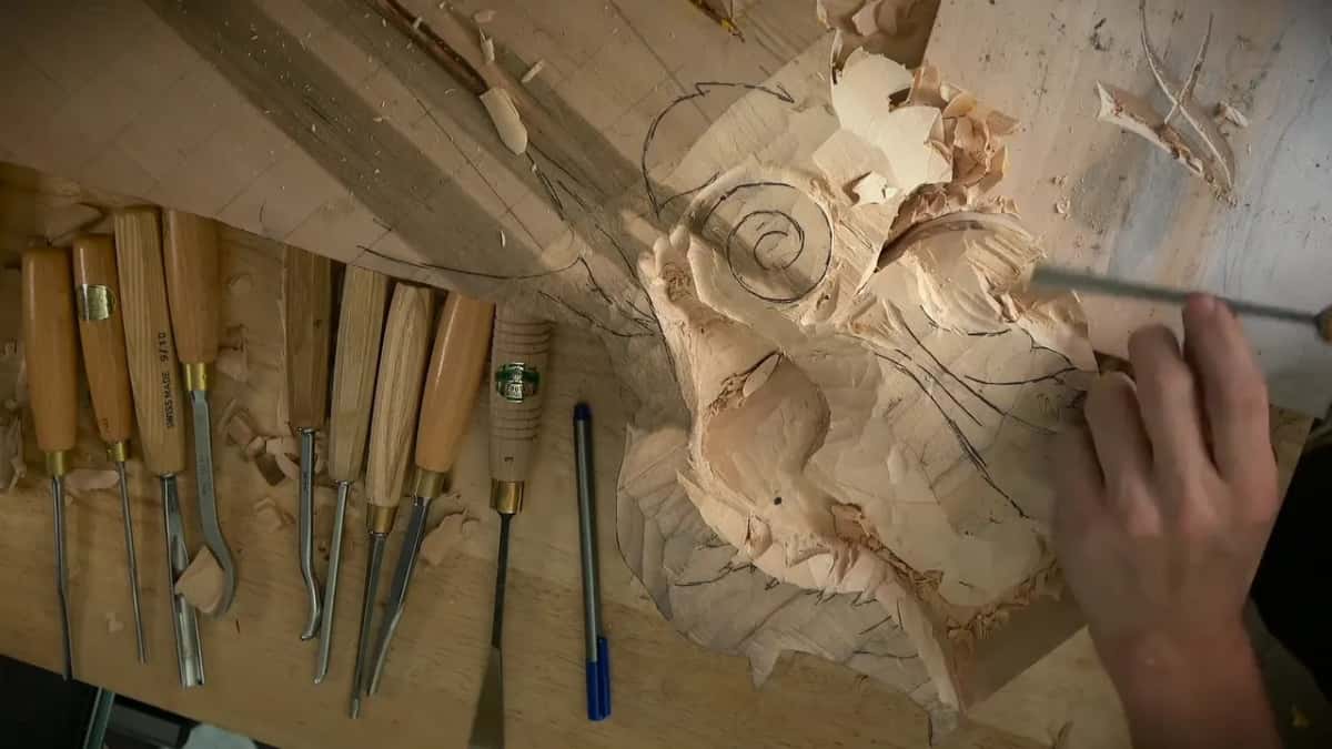 Right hand pushing a gouge over the top of the carved scroll, pencil guidelines still showing