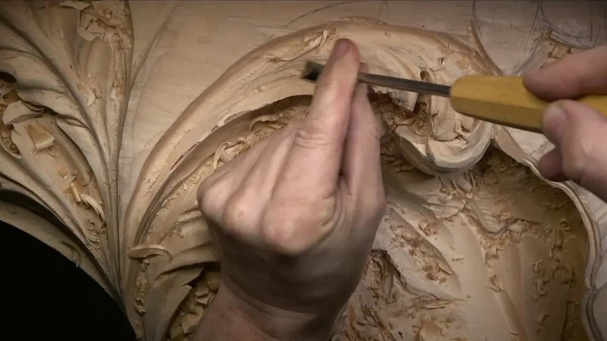 Fingers on the blade and a yellow handle steer the gouge across the leaf