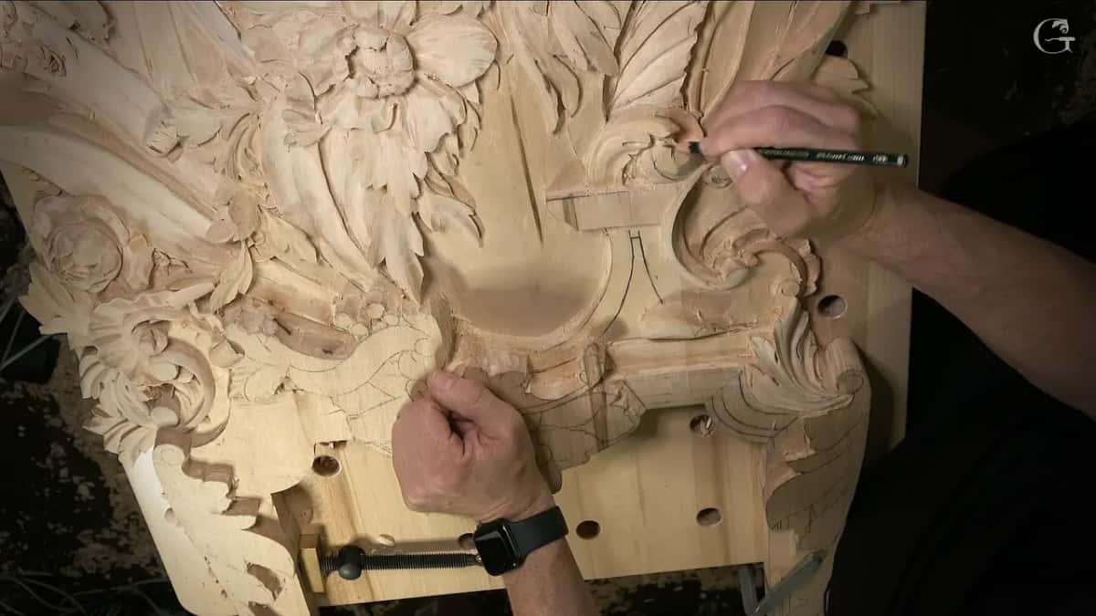 Wide view with a pencil drawing on the big leaf and the other hand resting on the carving