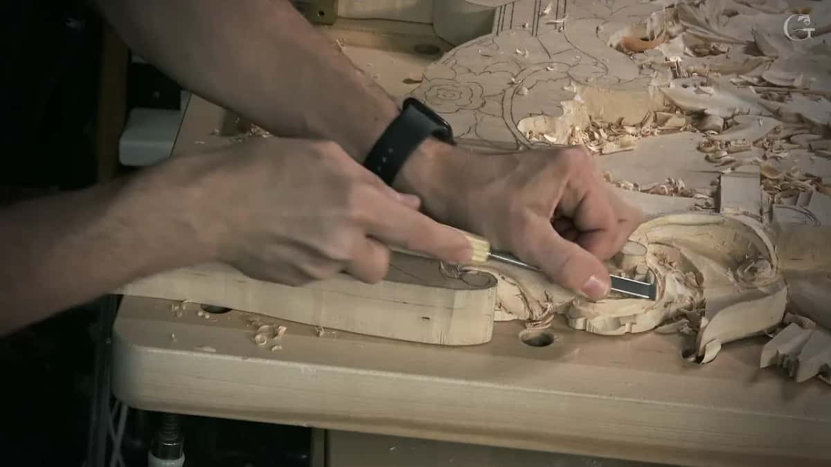 Seen from the side, two hands push a gouge down the slope of a leaf toward the board's edge