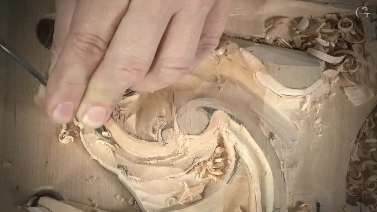 Thumb and two fingers steer a very thin veiner along an inner edge of the carving