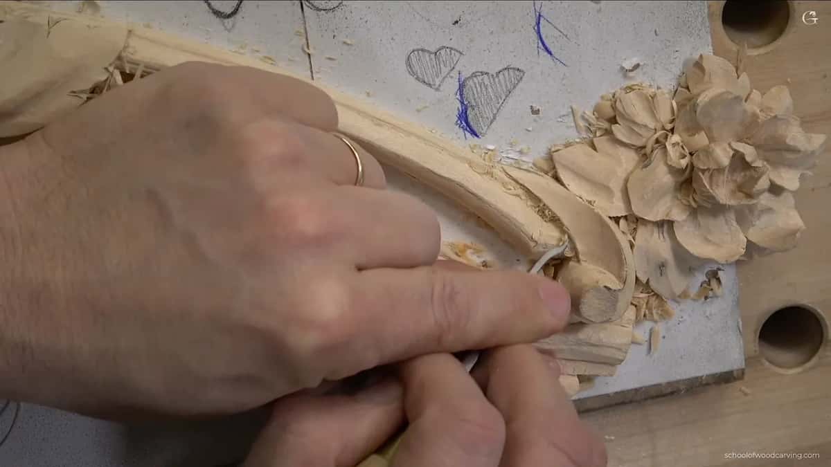 Fingers guide a small knife along the molding edge beside the flower