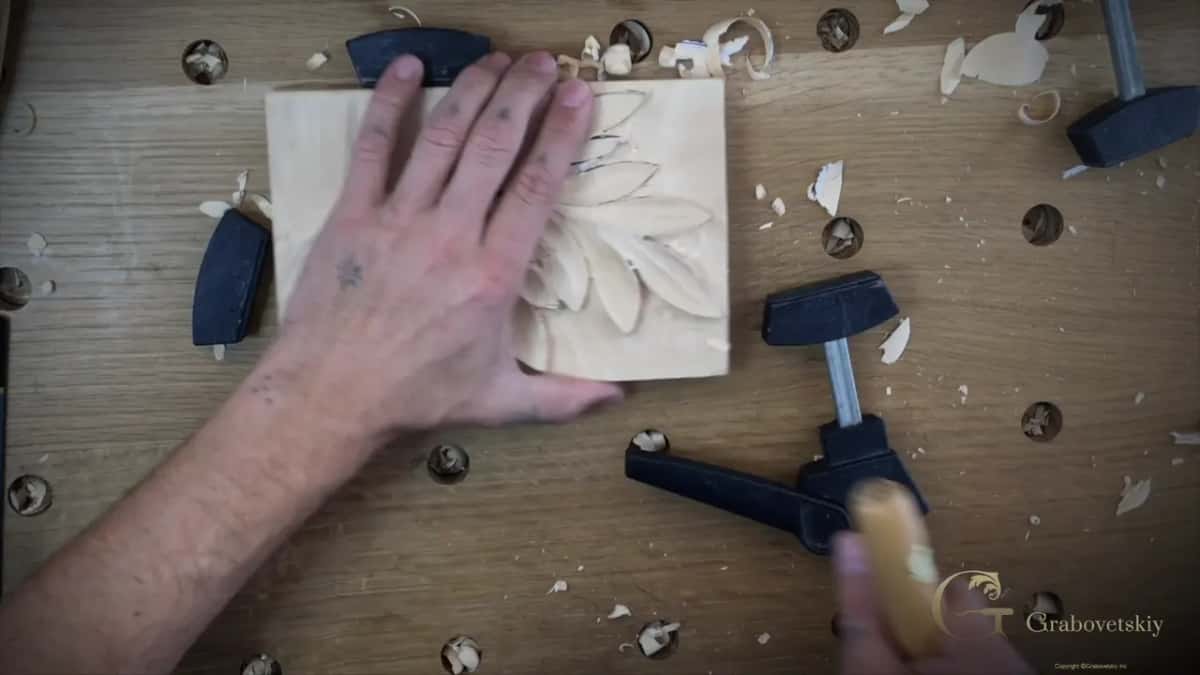 Square block with an acanthus leaf in relief, held at two corners by black screw clamps.