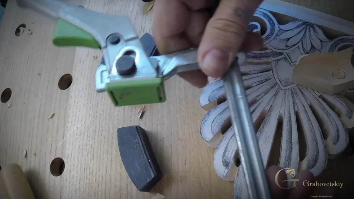 Green lever clamp lifted over a bench full of round holes, next to the half carved palmette and a gouge.