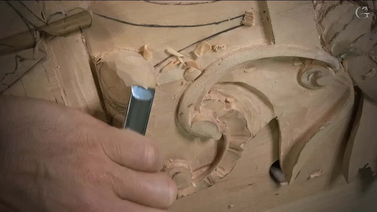 A wide flat gouge held over the scroll, its edge facing the wood