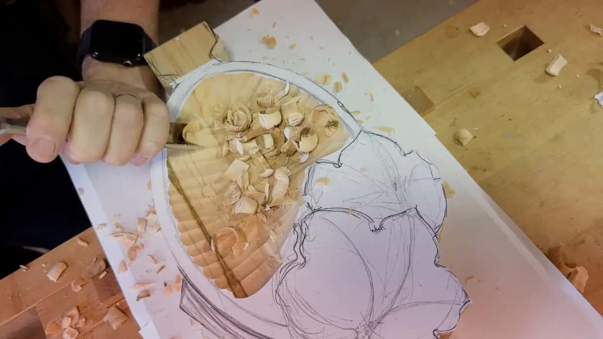 Closed fist around the gouge at the top of the hollow, curls piled on the paper and bench