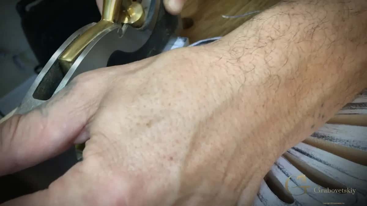 Shoulder plane in brass and steel under a flat hand, the paper swirls just beyond it