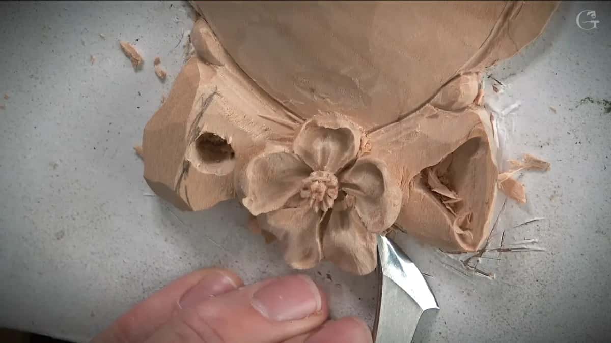 A curved blade works low under the flower toward the right loop, a thumb steadying it