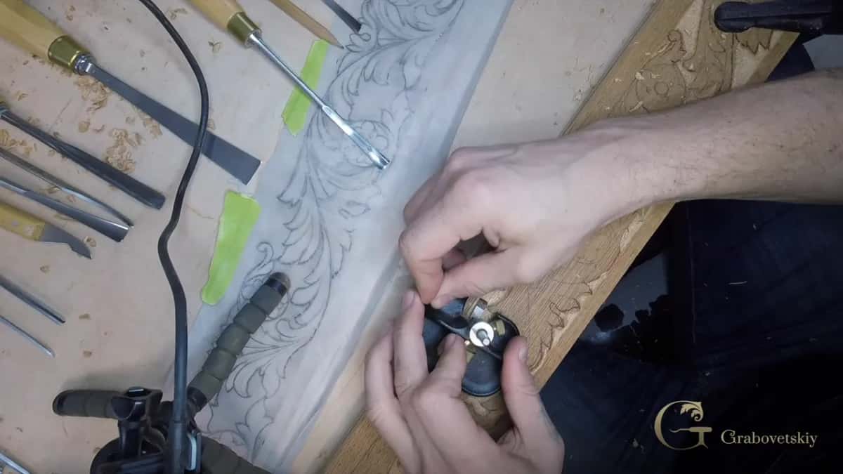 Small router plane held in two hands over the oak, with gouges and a power cord on the bench