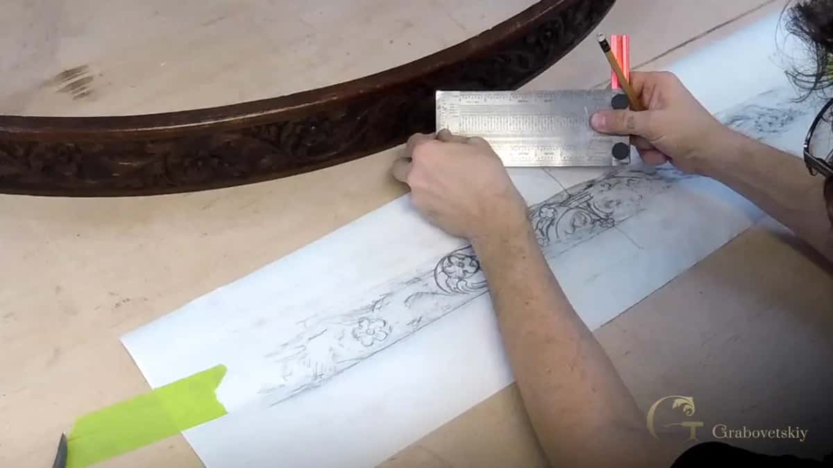 Hands hold a steel ruler and a pencil on the paper rubbing, the old apron lying just above