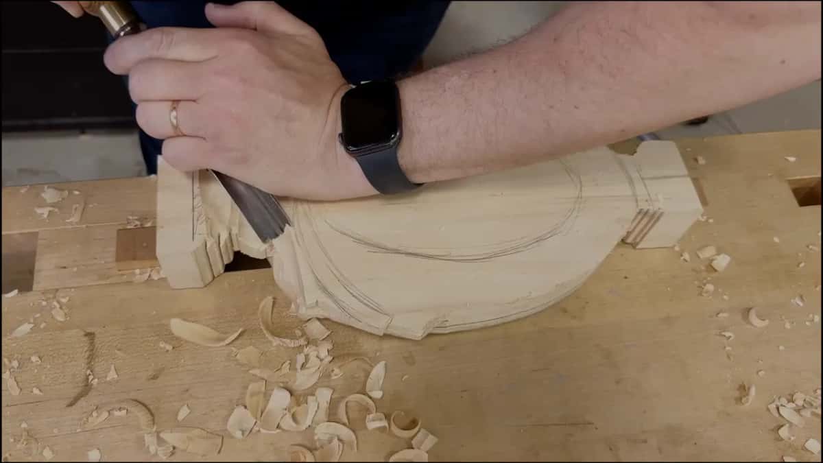 A hand pushes a gouge into the back beside the end block, curls of chips below