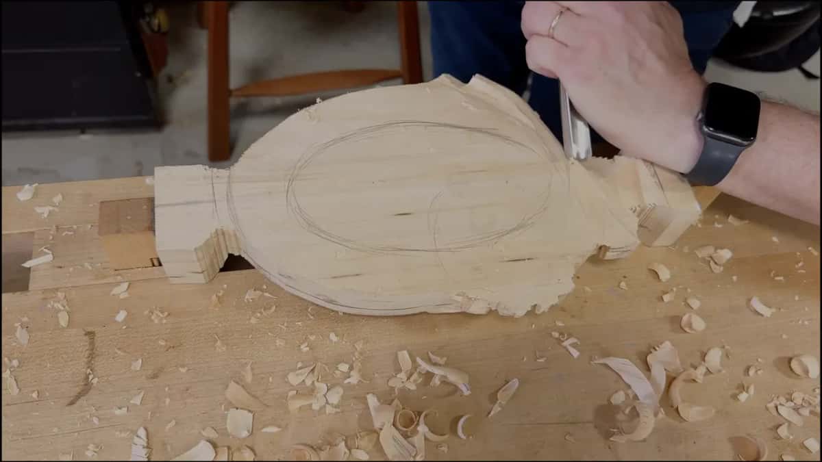 Hand and gouge at the leaf side of the upturned tray, the bowl outline drawn in pencil