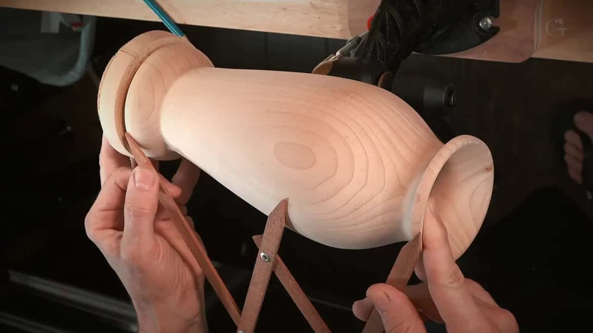 Three-legged calipers spanning foot to rim of a bare turned vase, the middle leg touching its widest part