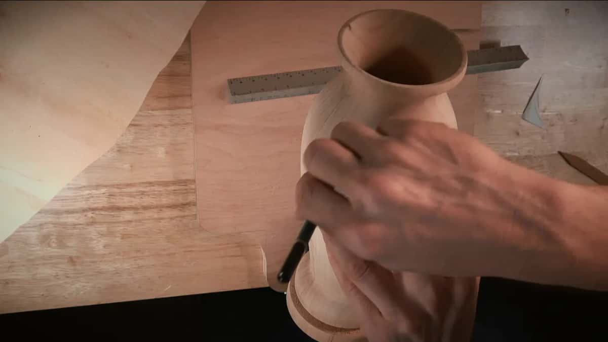 A paper disc pressed to the round body while a pencil follows its edge onto the bare wood