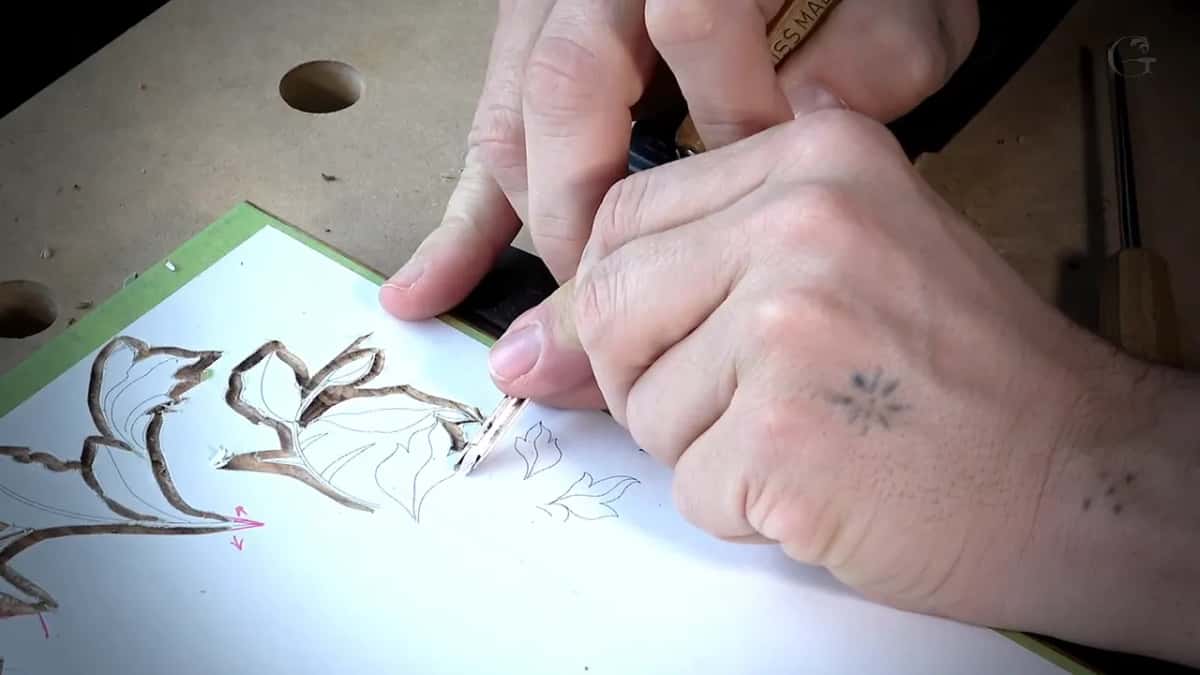 Two hands push a small gouge along a paper pattern on a board drilled with holes