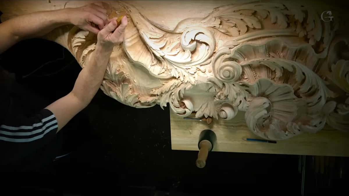 Arms reaching over a large acanthus carving fixed to a bench