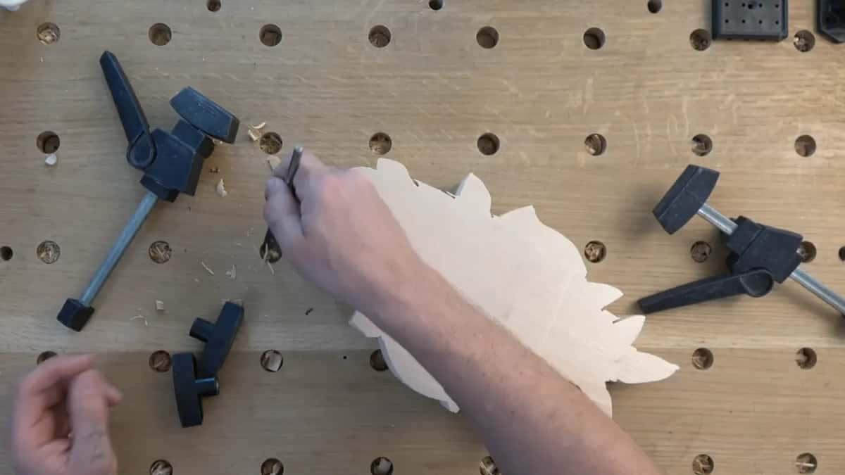 Seen from above, a small tool works the edge of a scalloped blank between black clamps on a holed top