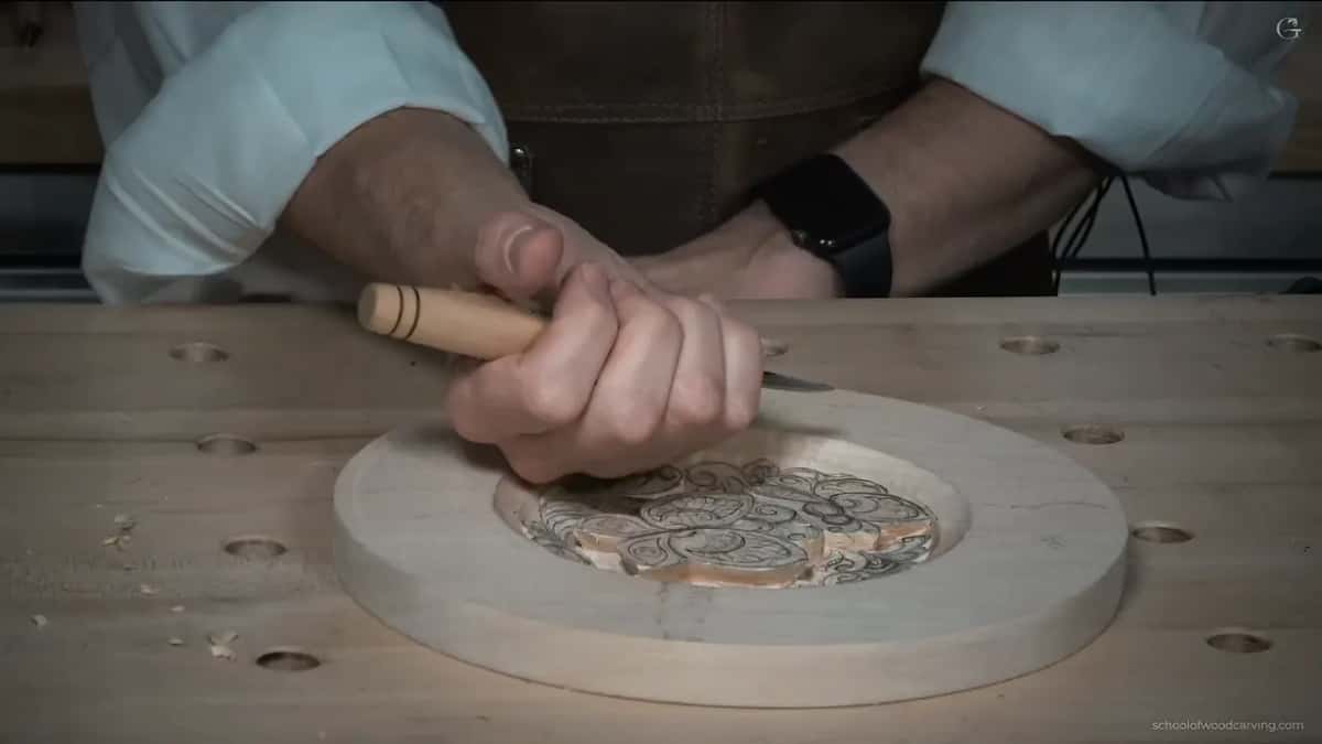 Fist around a short knife handle, the blade inside the rim of a round plate on a drilled bench top.