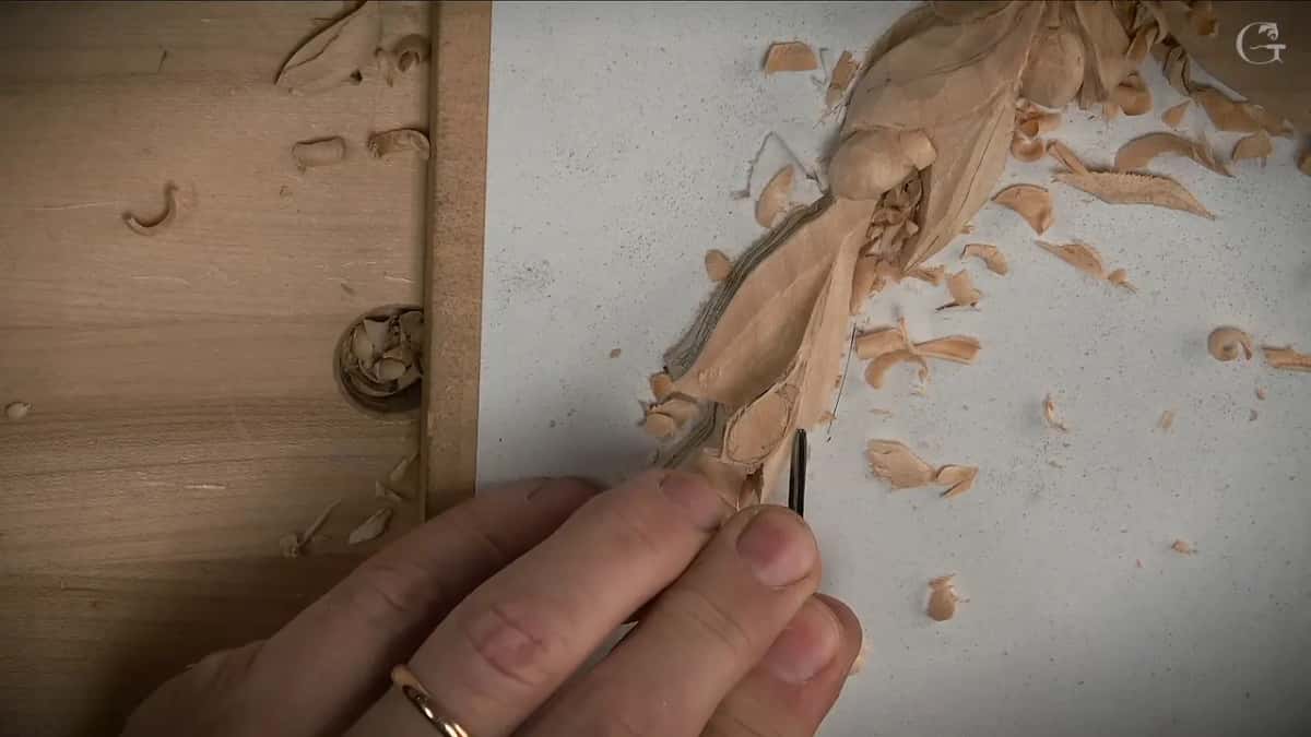Fingers holding a narrow tool upright against the carved form