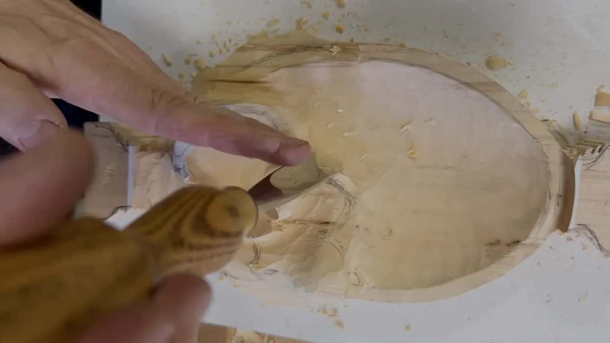 Fingertips on the leaf beside a gouge with a striped handle