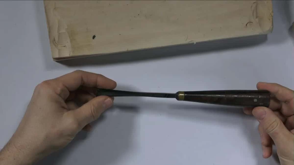 Two hands hold a dark handled gouge