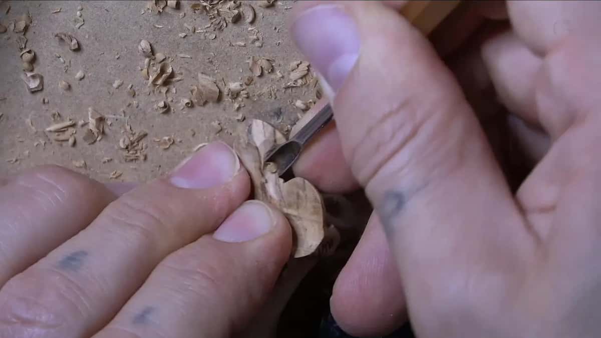 Two fingers hold a filler flower while a small gouge digs under one petal
