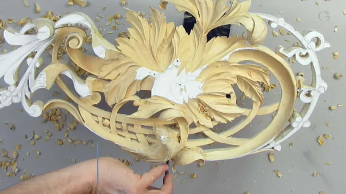 Fingers steady a pale pierced ornament with white on its outer scrolls while a small tool works inside