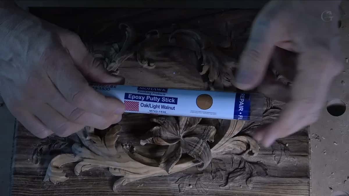 Mohawk epoxy putty stick, oak and light walnut, held over a dark carved panel