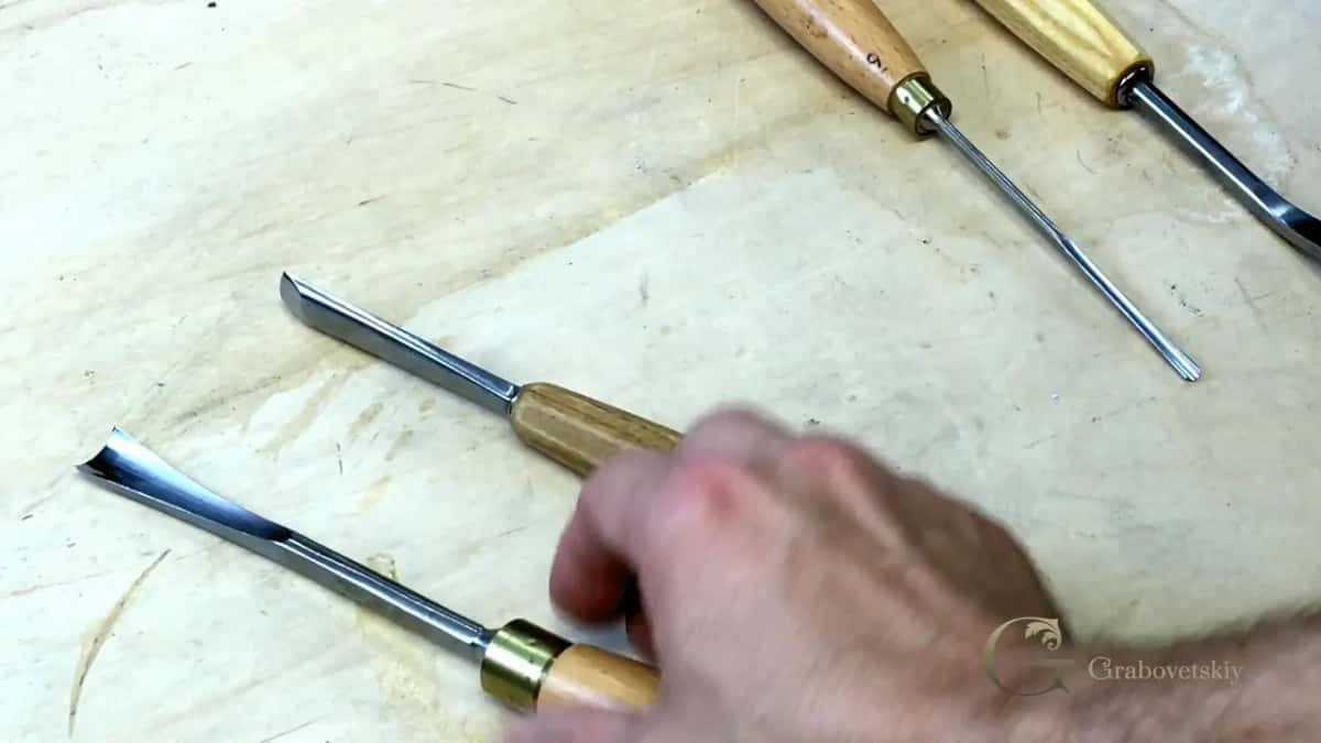 Four gouges on a pale board, a hand reaching for one