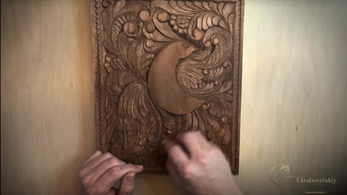 Right hand rubbing the lower carving of the stained board with a small piece held in the fingers