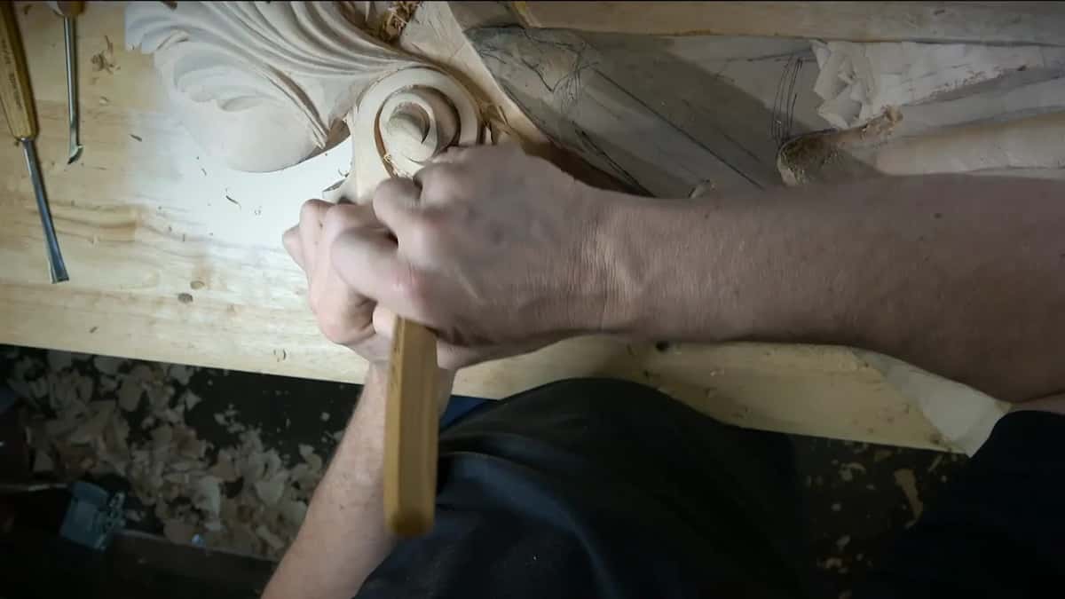 A fist wraps the handle at the scroll while more tools lie on the bench beyond it