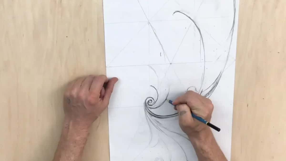 A hand pencils a scroll while the other holds the sheet