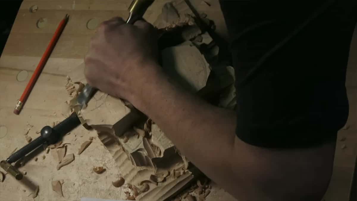 From above, a forearm and a gouge, with an orange pencil lying on the bench