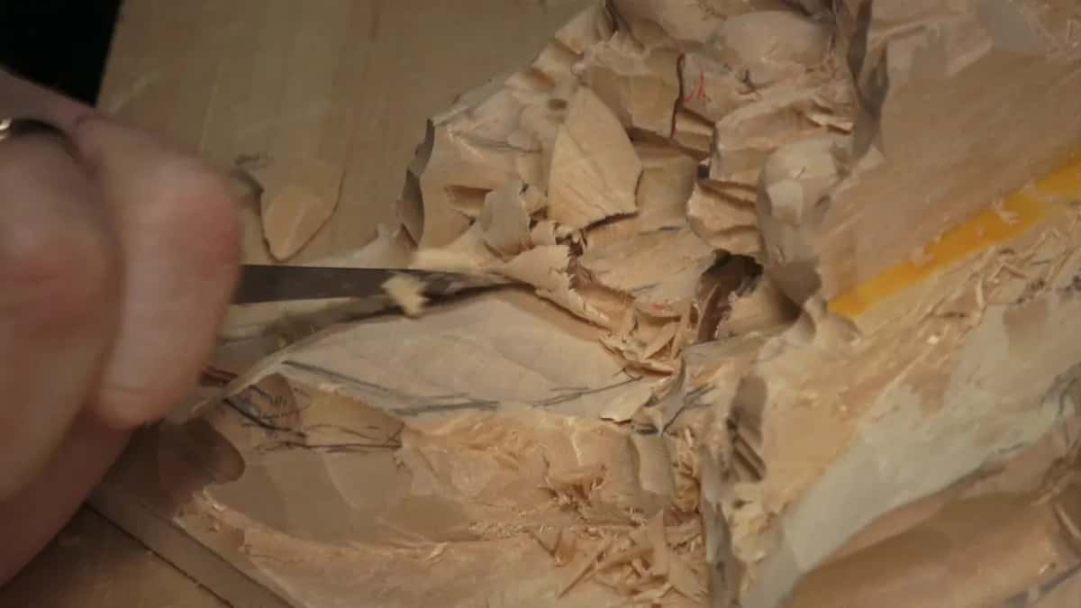 Close up of a gouge sliding down a pencil-marked slope, chips curling off its edge