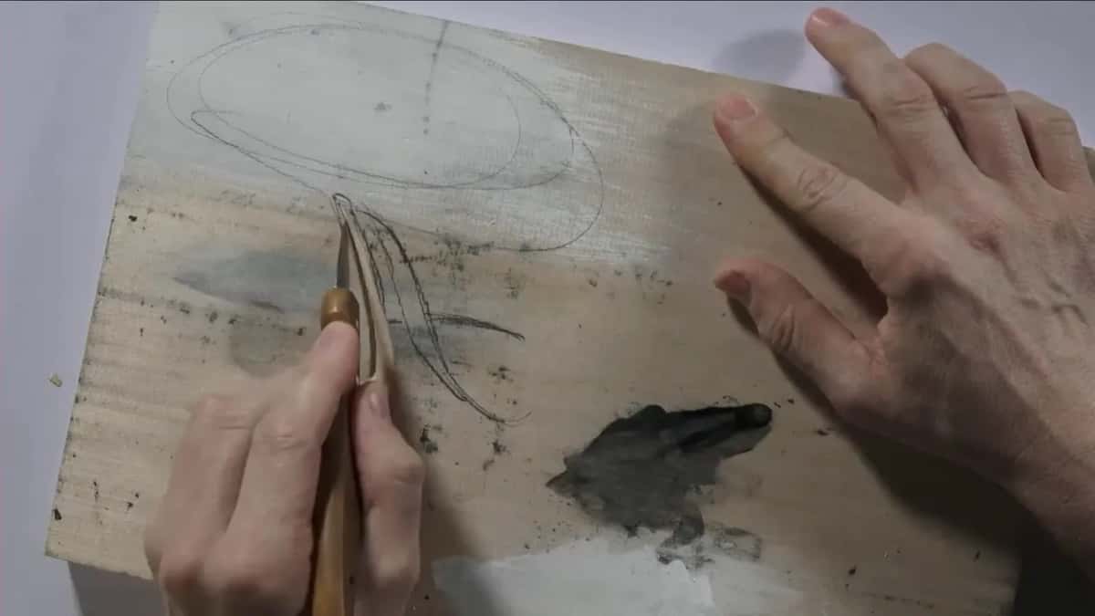 Blade standing upright in the carved stroke, the other hand spread out on the painted board beside a gray patch