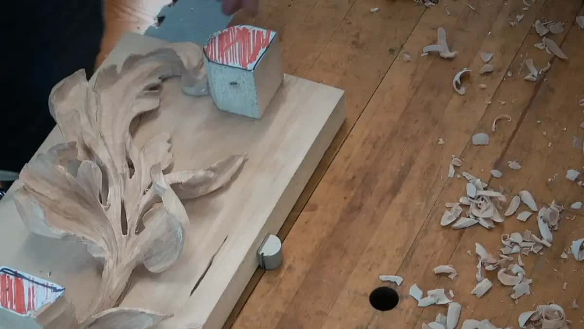 A blurred hand above the carved leaf, with chips scattered across the bench beside the board
