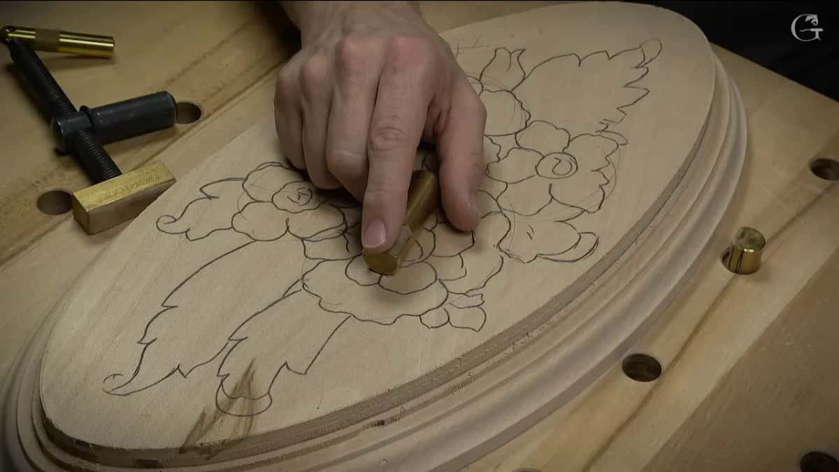 Brass dogs and a threaded clamp in the bench holes around an oval board drawn with roses