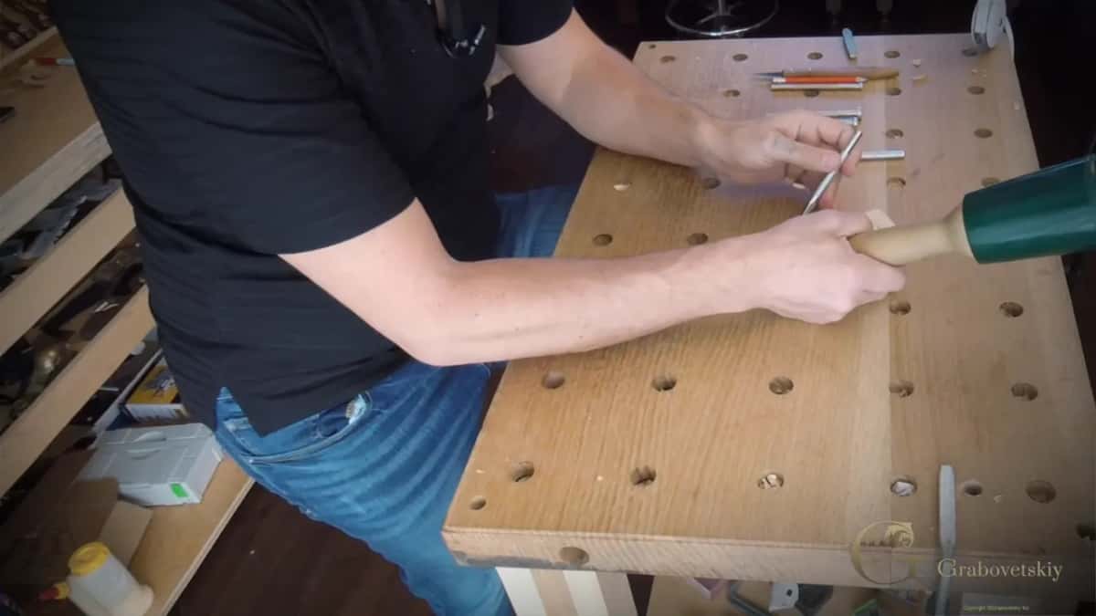 One hand on the mallet, the other holding a punch over a bench full of round holes