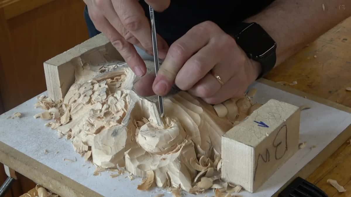 Both hands hold a narrow gouge straight up against the top of the round form