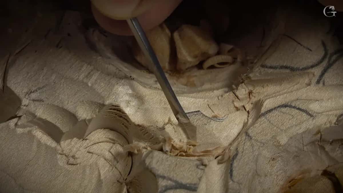 Below the cupped center, a fine tool works the bottom of a petal